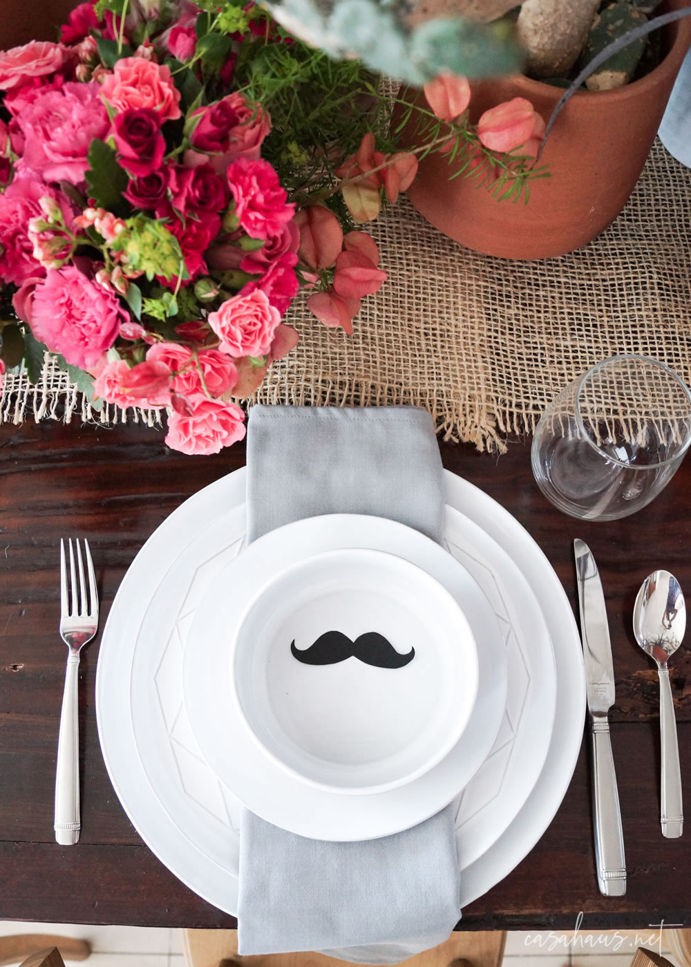 Platos puestos con bigote de papel, en mesa con cactus y flores rosas