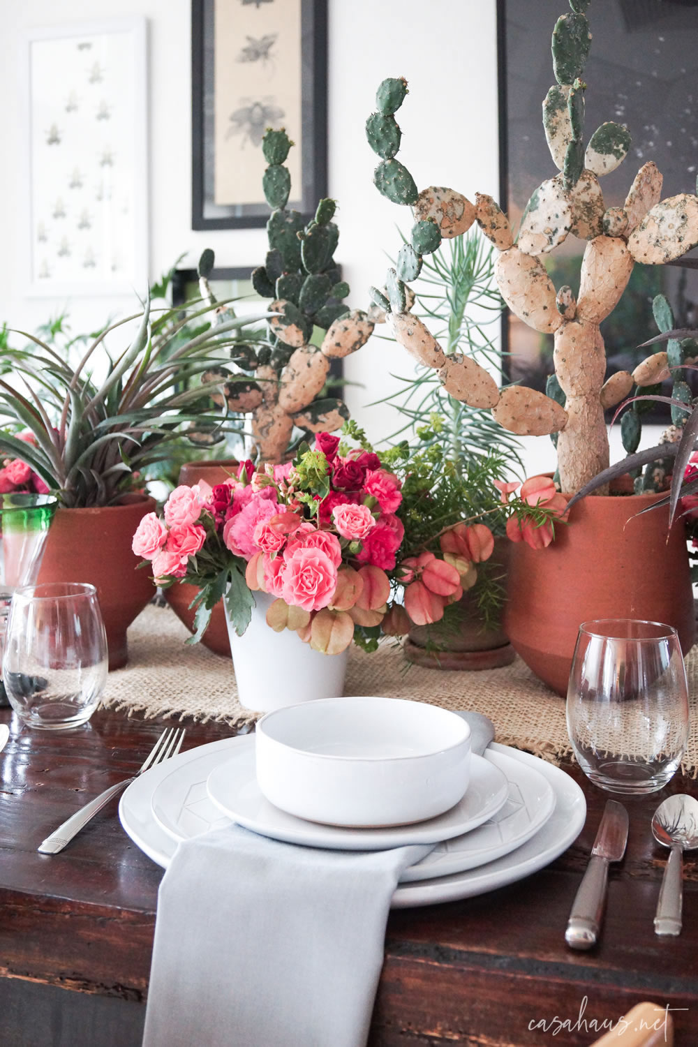Platos puestos en mesa con cactus y flores rosas